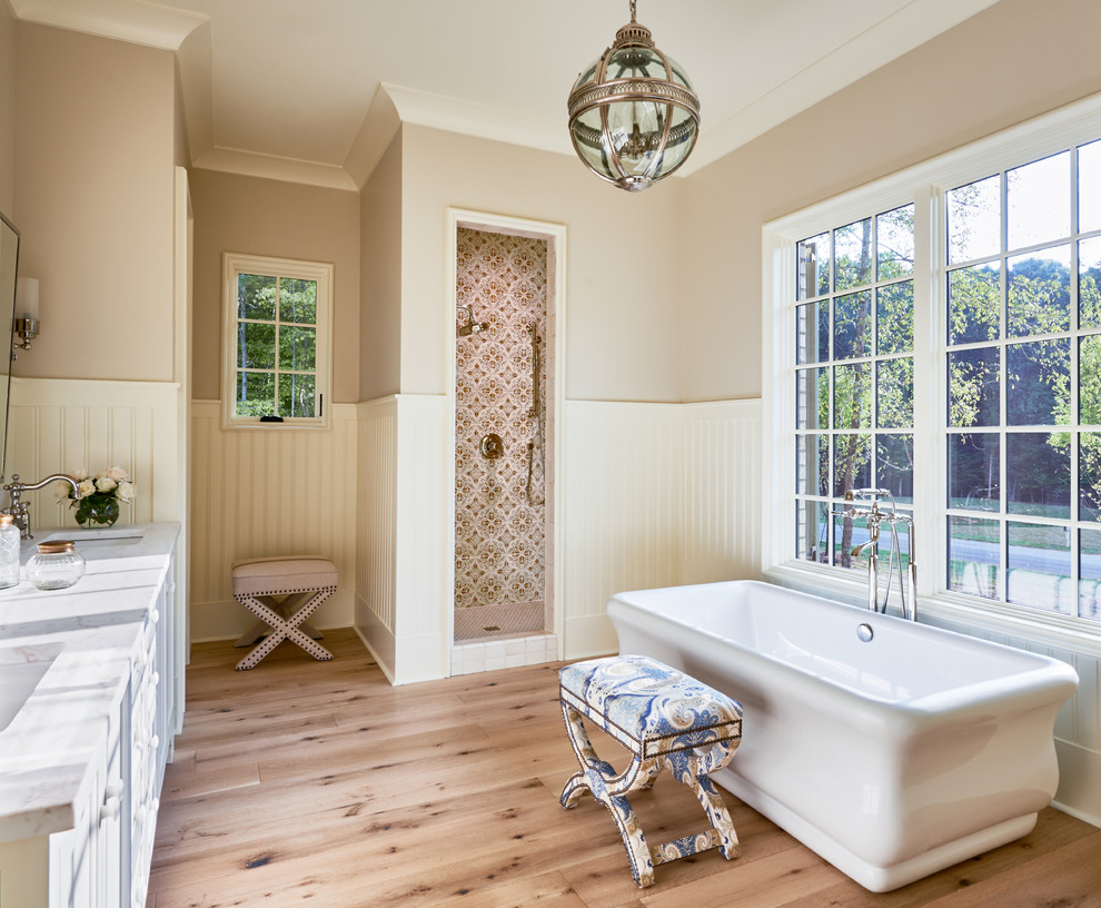 Design ideas for a traditional master bathroom in Charlotte with a freestanding tub, multi-coloured tile, beige walls and light hardwood floors.