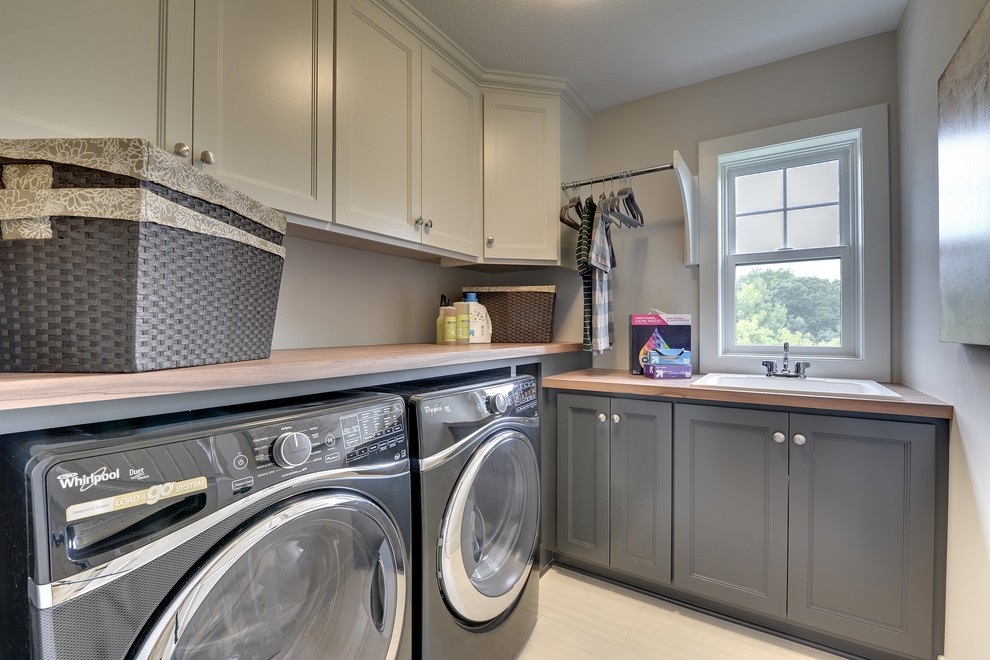 Design ideas for a large transitional l-shaped dedicated laundry room in Minneapolis with a drop-in sink, recessed-panel cabinets, grey cabinets, laminate benchtops, grey walls, ceramic floors and a side-by-side washer and dryer.