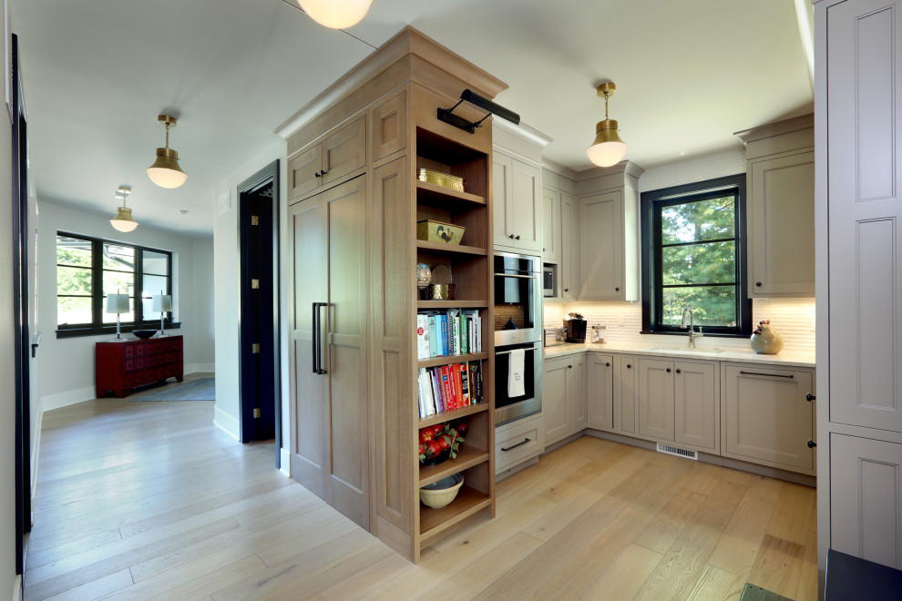 Design ideas for a mid-sized contemporary u-shaped kitchen pantry in Grand Rapids with a drop-in sink, recessed-panel cabinets, beige cabinets, marble benchtops, white splashback, stainless steel appliances, light hardwood floors, white benchtop and subway tile splashback.