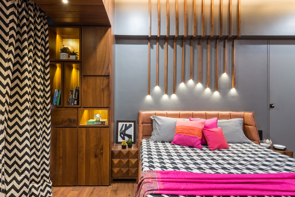 This is an example of a contemporary guest bedroom in Mumbai with grey walls, medium hardwood floors and brown floor.