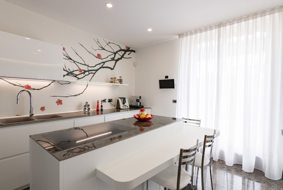 This is an example of a mid-sized contemporary galley separate kitchen in Milan with a double-bowl sink, flat-panel cabinets, white cabinets, quartz benchtops, white splashback, stainless steel appliances, porcelain floors, with island, brown floor and brown benchtop.