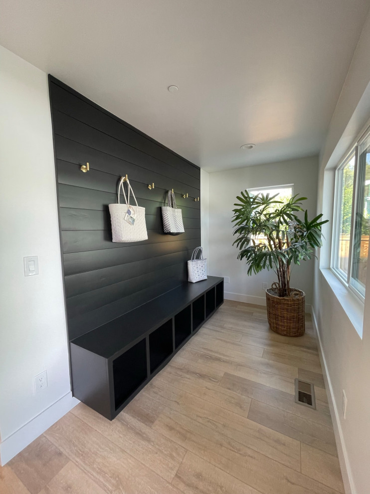Mid-sized country single-wall utility room in Sacramento with black cabinets, black splashback, shiplap splashback, white walls, light hardwood floors and brown floor.