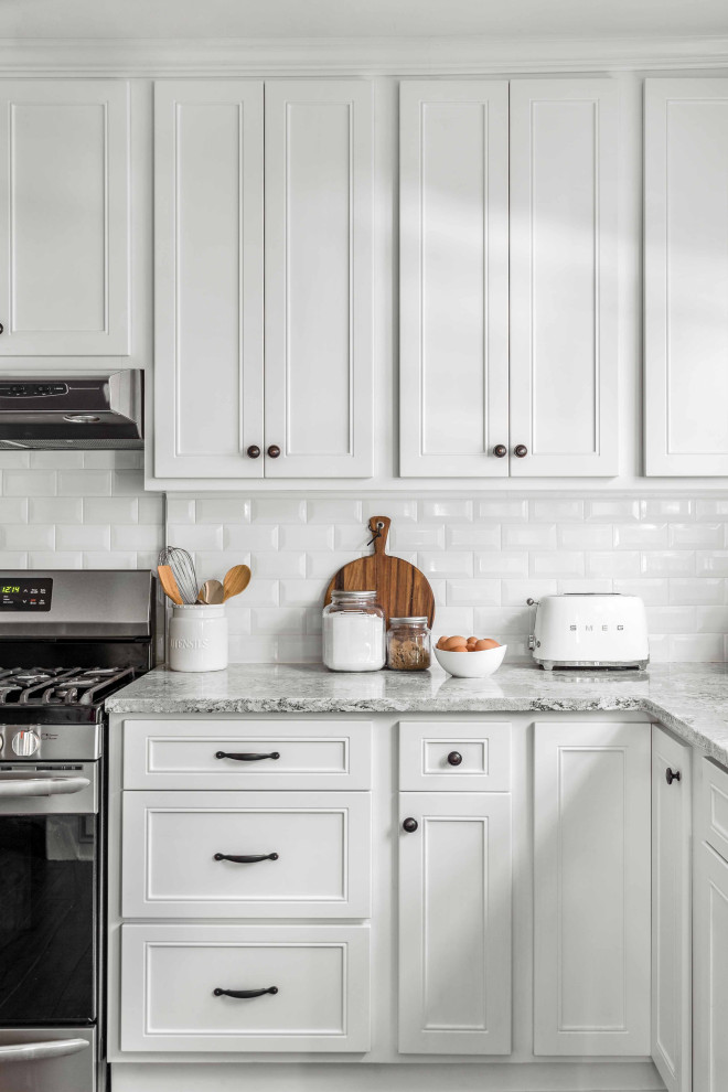 Example of a mid-sized cottage l-shaped porcelain tile and brown floor eat-in kitchen design in Philadelphia with a single-bowl sink, flat-panel cabinets, white cabinets, quartzite countertops, white backsplash, ceramic backsplash, stainless steel appliances and gray countertops