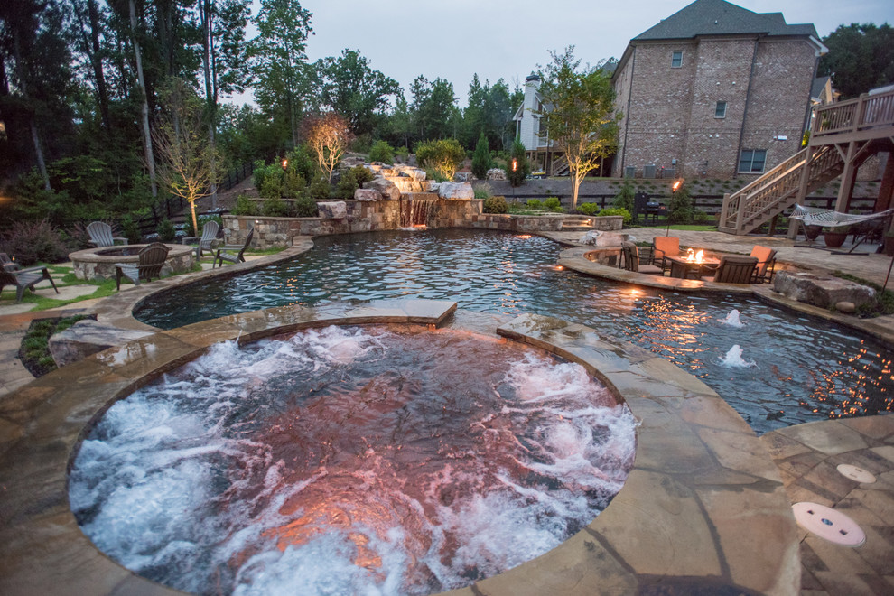 Design ideas for an expansive tropical backyard custom-shaped natural pool in Atlanta with a hot tub and natural stone pavers.