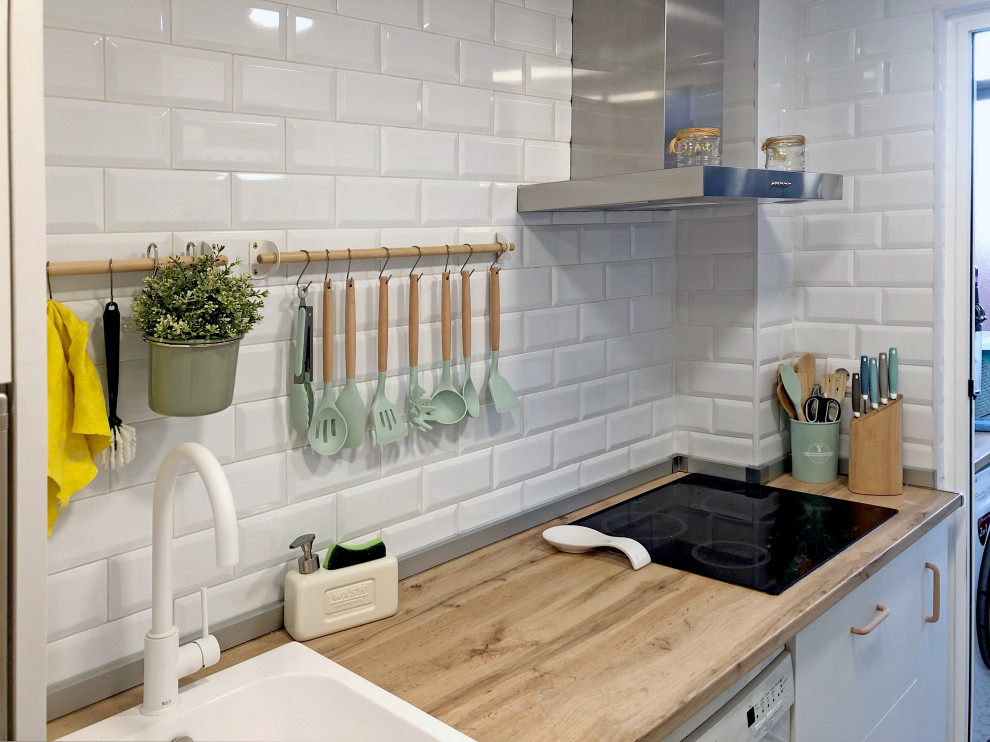 Foto på ett avskilt, litet skandinaviskt brun kök, med en undermonterad diskho, släta luckor, vita skåp, träbänkskiva, vitt stänkskydd, stänkskydd i keramik, rostfria vitvaror, klinkergolv i keramik och flerfärgat golv