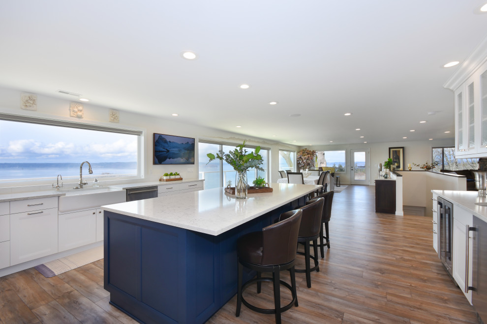 Large transitional u-shaped open plan kitchen in Seattle with a farmhouse sink, shaker cabinets, white cabinets, quartz benchtops, grey splashback, glass tile splashback, stainless steel appliances, vinyl floors, with island, multi-coloured floor and white benchtop.