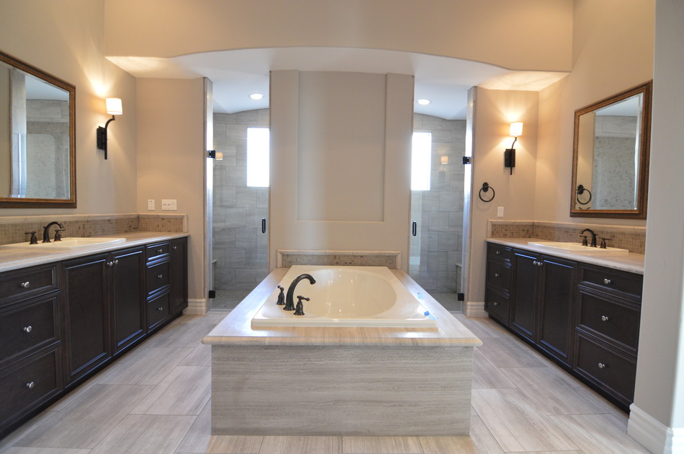 This is an example of a large contemporary bathroom in Orange County with recessed-panel cabinets, dark wood cabinets, granite benchtops, a drop-in tub, a double shower, gray tile, wood-look tile and beige walls.