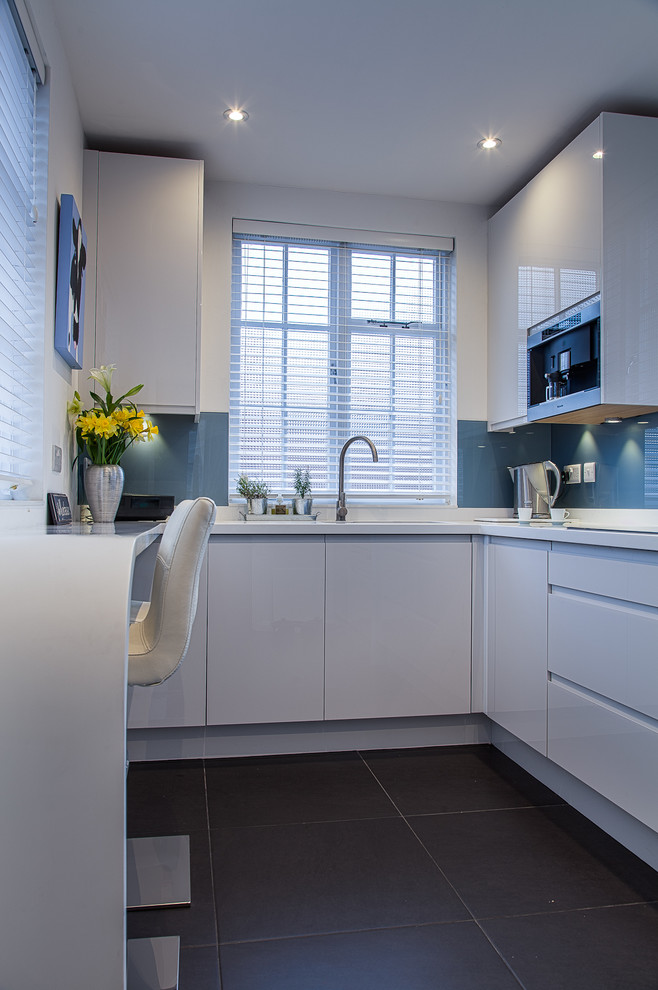 Small contemporary u-shaped eat-in kitchen in Hertfordshire with an undermount sink, flat-panel cabinets, white cabinets, solid surface benchtops, blue splashback, stainless steel appliances, porcelain floors and a peninsula.