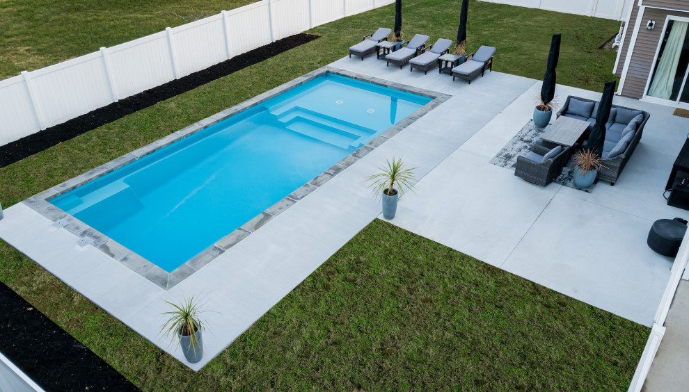 Modelo de piscina alargada contemporánea grande rectangular en patio trasero con paisajismo de piscina y adoquines de ladrillo