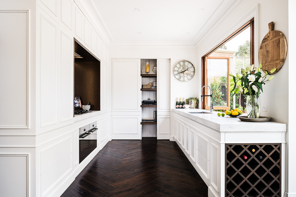 Inspiration for a large traditional u-shaped separate kitchen in Melbourne with white cabinets, marble benchtops, dark hardwood floors, brown floor, an undermount sink, black appliances, raised-panel cabinets, white splashback, marble splashback and no island.
