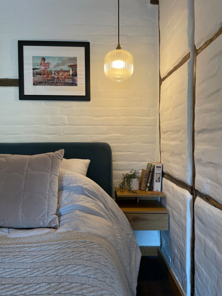 Cette image montre une petite chambre parentale design avec un mur beige, parquet foncé, une cheminée standard, un manteau de cheminée en brique, un sol marron, poutres apparentes et un mur en parement de brique.