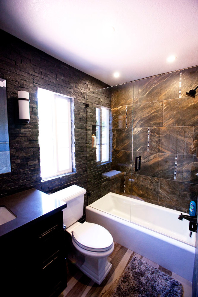 This is an example of a mid-sized transitional bathroom in Los Angeles with shaker cabinets, dark wood cabinets, an alcove tub, an alcove shower, a two-piece toilet, brown tile, porcelain tile, brown walls, dark hardwood floors, an undermount sink, engineered quartz benchtops, brown floor and a hinged shower door.