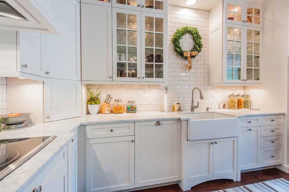 This is an example of a traditional kitchen in Orlando with a farmhouse sink, glass-front cabinets, beige cabinets, marble benchtops, beige splashback and subway tile splashback.