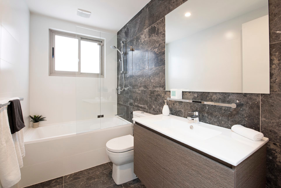This is an example of a mid-sized modern master bathroom in Sydney with a shower/bathtub combo, multi-coloured tile, flat-panel cabinets, dark wood cabinets, an alcove tub, a two-piece toilet, white walls, an integrated sink, brown floor and a hinged shower door.