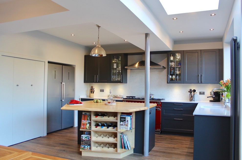 This is an example of a mid-sized eclectic l-shaped open plan kitchen in London with a drop-in sink, shaker cabinets, black cabinets, quartzite benchtops, grey splashback, coloured appliances, vinyl floors, with island and brown floor.