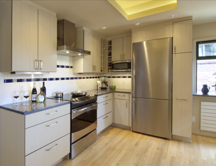 This is an example of a mid-sized modern l-shaped eat-in kitchen in Seattle with an undermount sink, flat-panel cabinets, light wood cabinets, quartz benchtops, white splashback, ceramic splashback, stainless steel appliances, light hardwood floors and a peninsula.