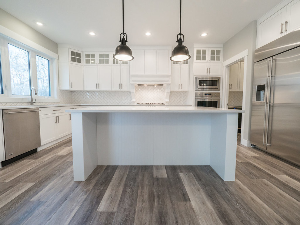 Photo of a mid-sized traditional u-shaped eat-in kitchen in Edmonton with a double-bowl sink, recessed-panel cabinets, white cabinets, quartzite benchtops, white splashback, subway tile splashback, stainless steel appliances, vinyl floors, with island and multi-coloured floor.