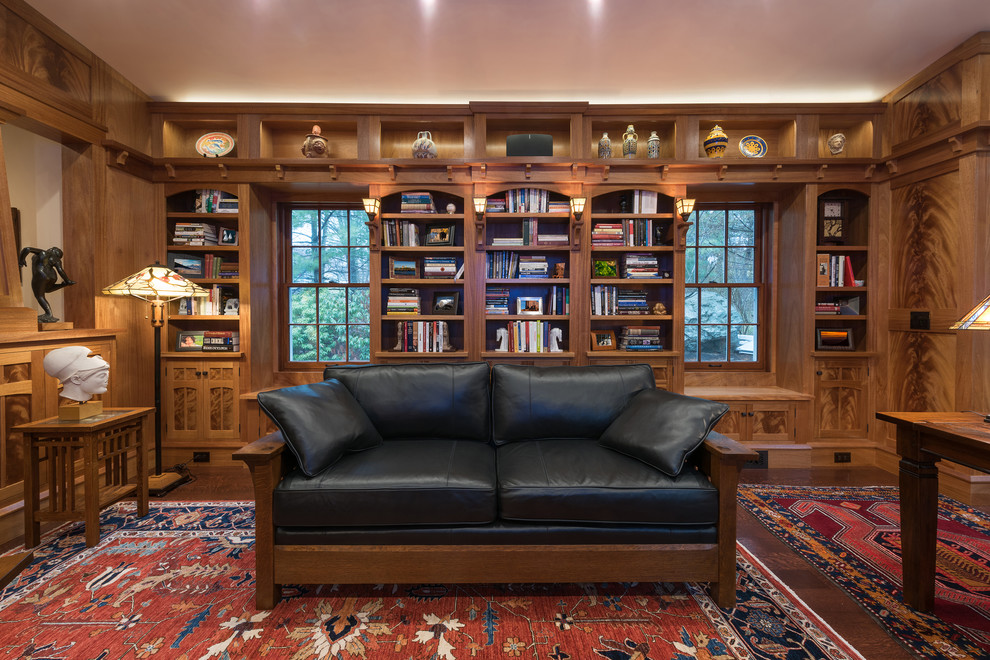 This is an example of an arts and crafts home office in Boston with a library, brown walls, dark hardwood floors, a freestanding desk and brown floor.