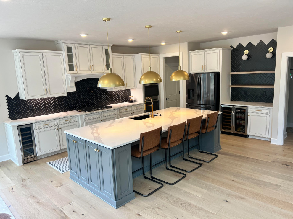 Example of a transitional kitchen design with shaker cabinets, white cabinets, quartz countertops, black backsplash and an island