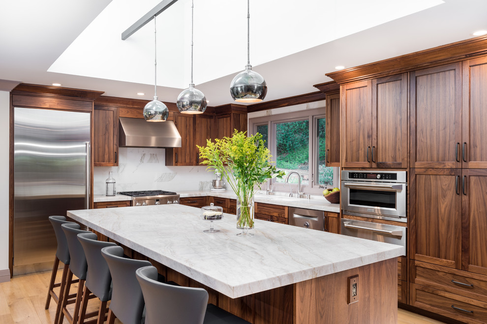 Design ideas for a transitional l-shaped open plan kitchen in San Francisco with an undermount sink, recessed-panel cabinets, medium wood cabinets, marble benchtops, white splashback, stainless steel appliances, light hardwood floors, with island and beige floor.