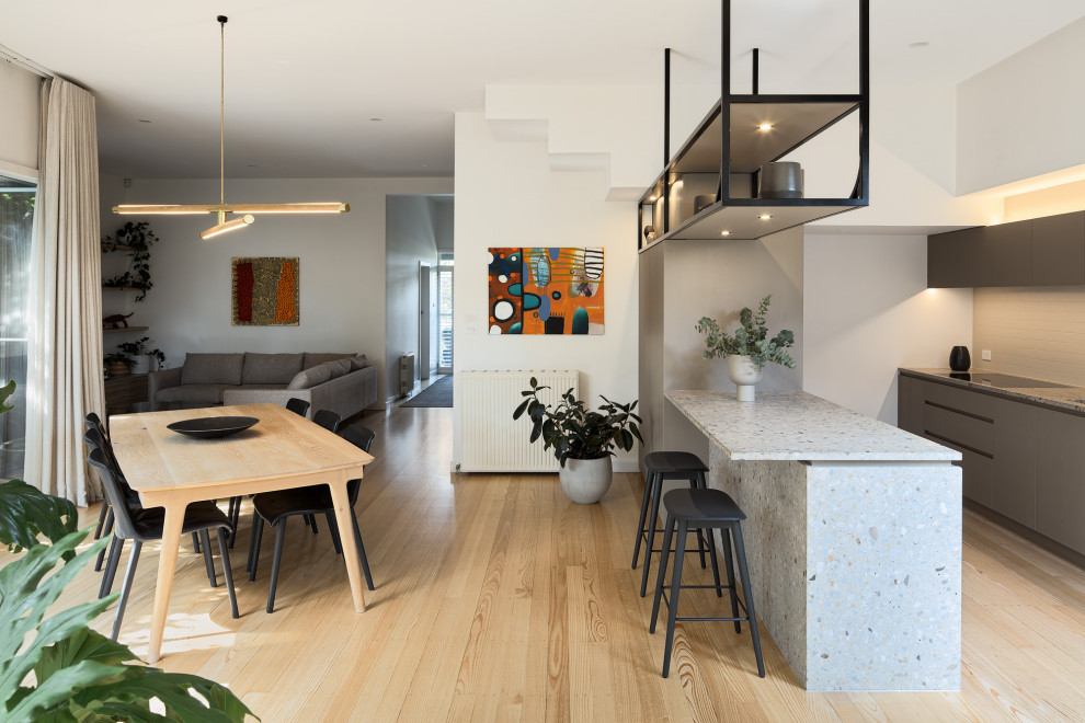 This is an example of a small contemporary eat-in kitchen in Melbourne with a double-bowl sink, flat-panel cabinets, grey cabinets, terrazzo benchtops, grey splashback, ceramic splashback, black appliances, light hardwood floors, with island and multi-coloured benchtop.
