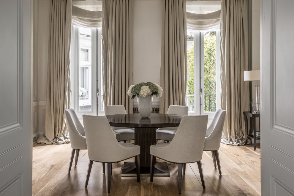 Photo of a large transitional separate dining room in London with white walls, medium hardwood floors, a standard fireplace, a stone fireplace surround, brown floor and panelled walls.