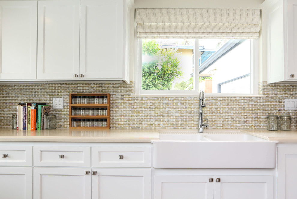 This is an example of a mid-sized transitional galley open plan kitchen in Los Angeles with a farmhouse sink, shaker cabinets, white cabinets, solid surface benchtops, green splashback, glass tile splashback, stainless steel appliances, medium hardwood floors and with island.