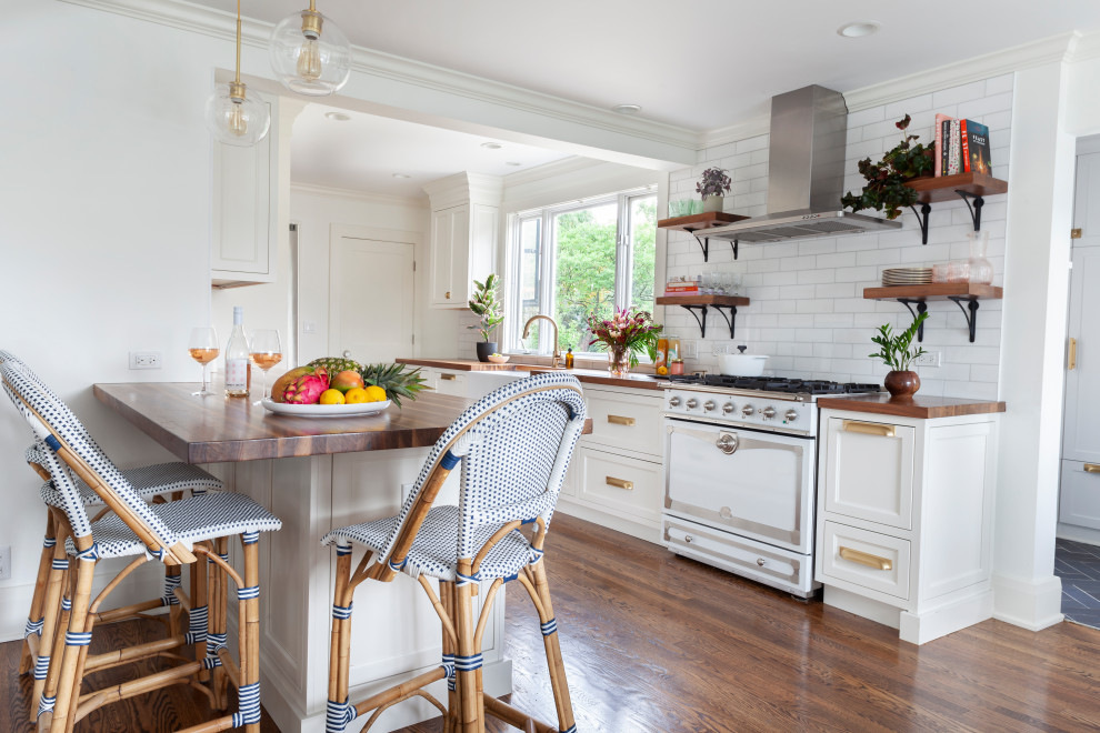 Eat-in kitchen - large eclectic galley medium tone wood floor and brown floor eat-in kitchen idea in Chicago with a farmhouse sink, recessed-panel cabinets, white cabinets, wood countertops, white backsplash, subway tile backsplash, stainless steel appliances, an island and brown countertops