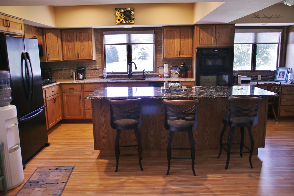 Eat-in kitchen - mid-sized l-shaped eat-in kitchen idea with flat-panel cabinets, medium tone wood cabinets, quartz countertops, beige backsplash, black appliances and an island