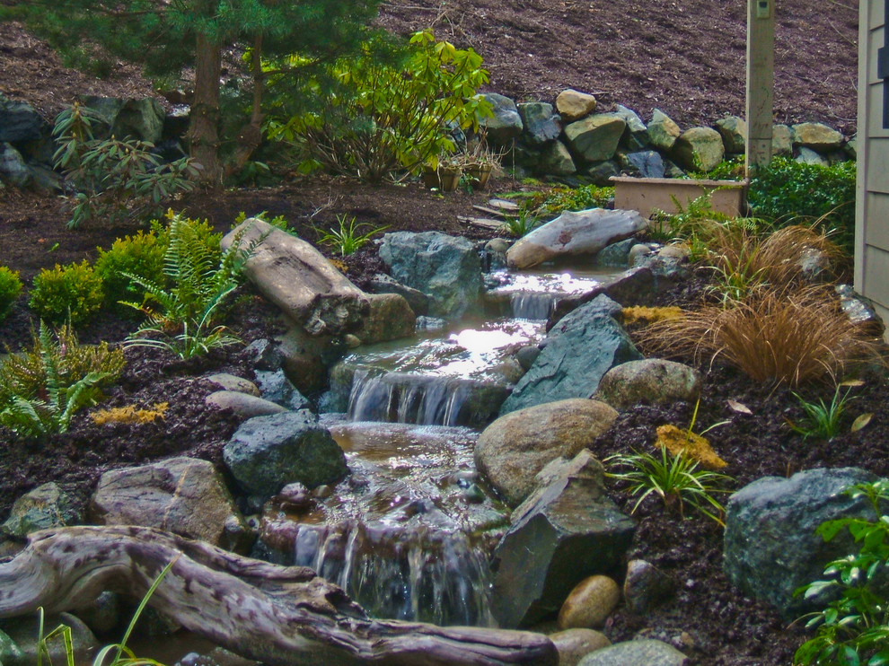 Photo of a mid-sized rustic full sun backyard stone water fountain landscape in Seattle for spring.
