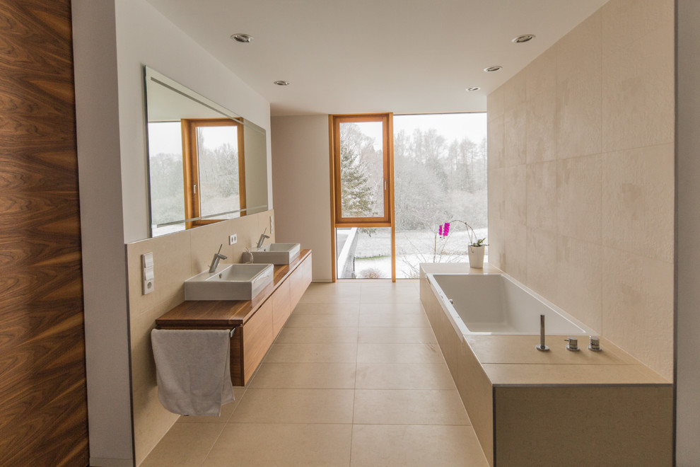 Modern bathroom in Other with a vessel sink, a drop-in tub, a curbless shower, beige tile and stone tile.