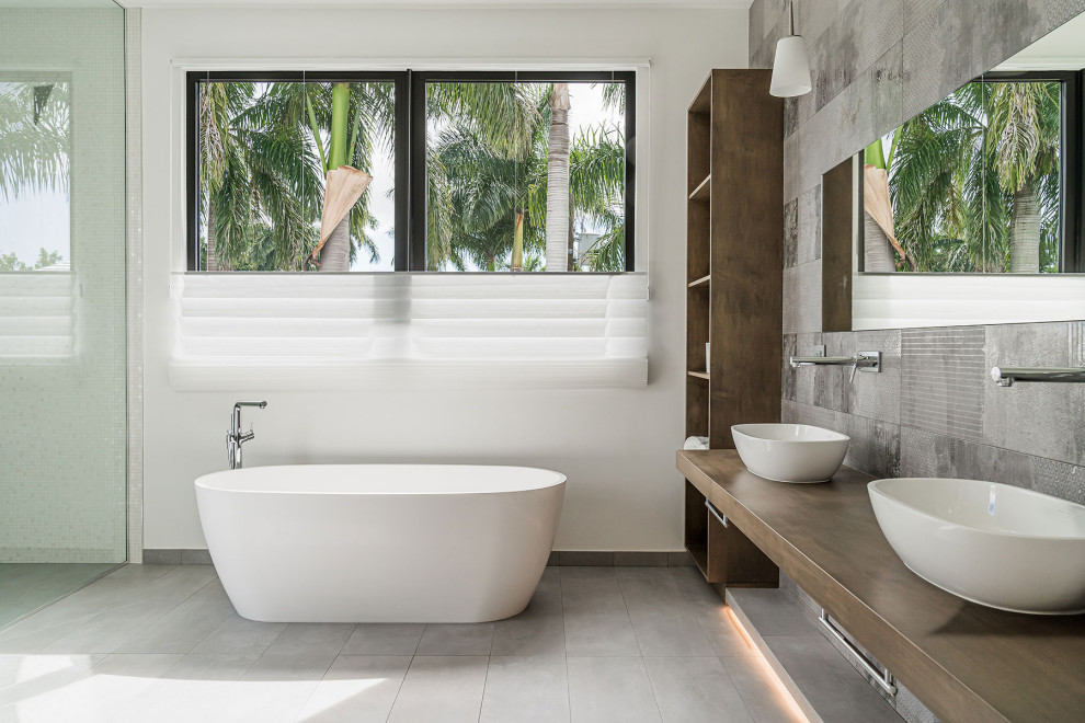 Пример оригинального дизайна: большая главная ванная комната в современном стиле с отдельно стоящей ванной, керамической плиткой, белыми стенами, полом из керамической плитки, серым полом, коричневой столешницей, тумбой под две раковины и встроенной тумбой