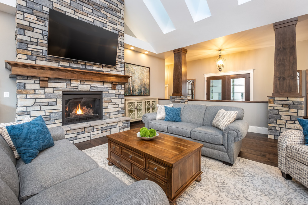 Photo of a large traditional open concept living room in Other with grey walls, dark hardwood floors, a standard fireplace, a stone fireplace surround, a wall-mounted tv and brown floor.