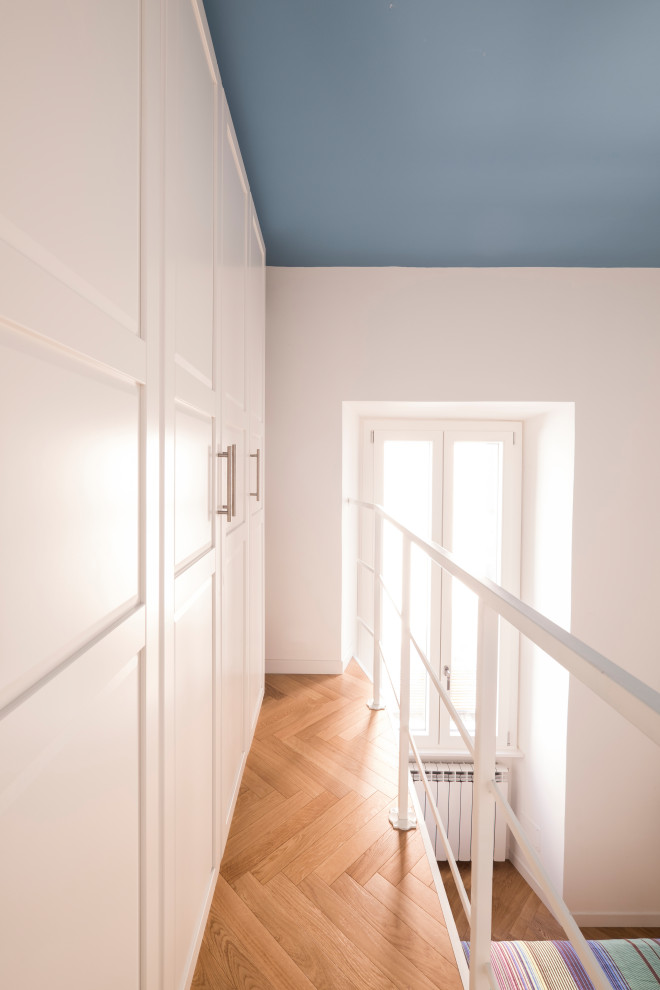 This is an example of a small eclectic gender neutral standard wardrobe in Rome with recessed-panel cabinets, white cabinets and light hardwood flooring.