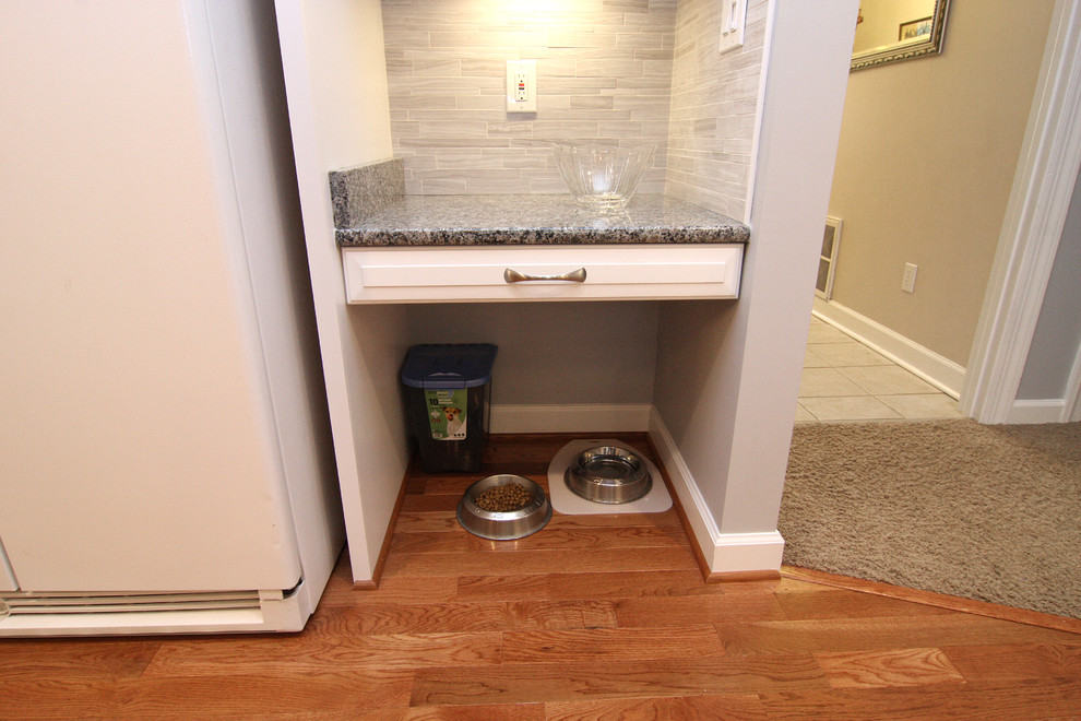 Example of a mid-sized transitional u-shaped medium tone wood floor eat-in kitchen design with an undermount sink, raised-panel cabinets, white cabinets, granite countertops, gray backsplash, porcelain backsplash, white appliances and an island