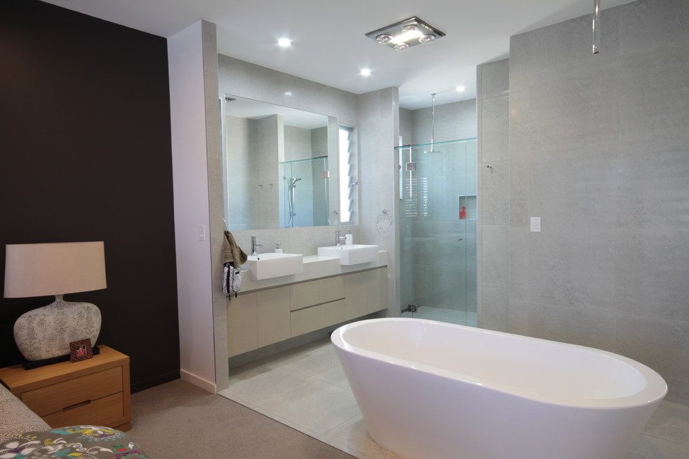 Photo of a mid-sized contemporary master bathroom in Sunshine Coast with a vessel sink, flat-panel cabinets, light wood cabinets, engineered quartz benchtops, a freestanding tub, an alcove shower, a wall-mount toilet, gray tile, porcelain tile, grey walls and porcelain floors.