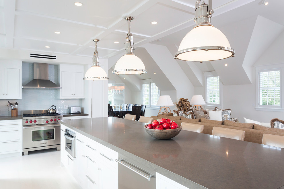 Large beach style l-shaped open plan kitchen in Boston with stainless steel appliances, an undermount sink, shaker cabinets, white cabinets, grey splashback, with island and white floor.