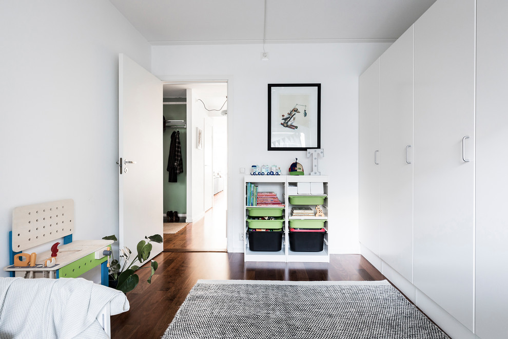 This is an example of a mid-sized scandinavian gender-neutral kids' room in Stockholm with white walls and dark hardwood floors.