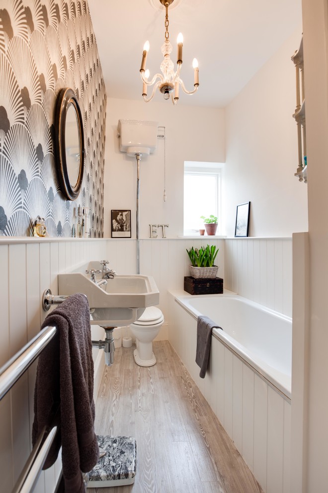 Small traditional bathroom in Hampshire with a wall-mount sink, a drop-in tub, a two-piece toilet, multi-coloured walls and light hardwood floors.
