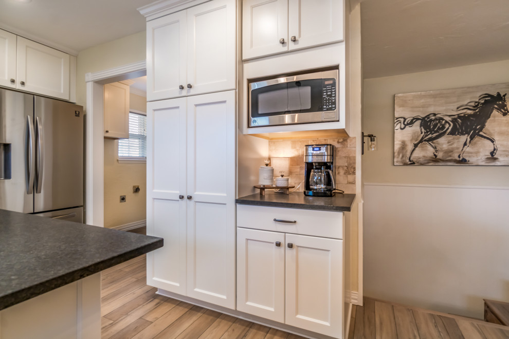 Transitional galley vinyl floor and beige floor eat-in kitchen photo with a double-bowl sink, recessed-panel cabinets, white cabinets, granite countertops, beige backsplash, travertine backsplash, stainless steel appliances, a peninsula and black countertops