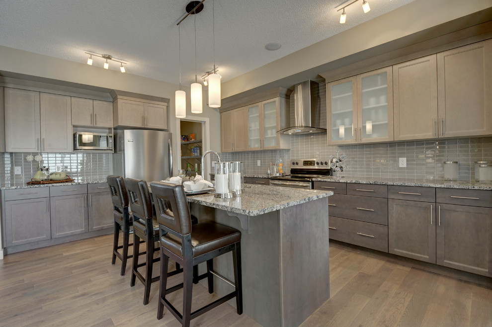 Mid-sized transitional l-shaped medium tone wood floor and brown floor eat-in kitchen photo in Edmonton with a double-bowl sink, shaker cabinets, brown cabinets, granite countertops, gray backsplash, ceramic backsplash, stainless steel appliances and an island