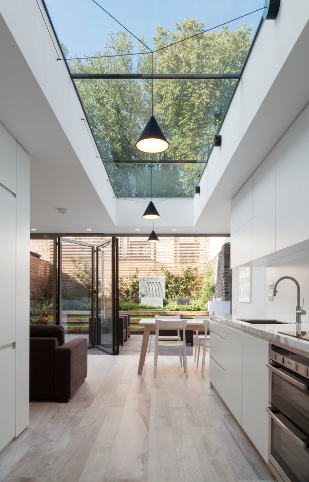 This is an example of a contemporary galley kitchen in London with an undermount sink, flat-panel cabinets, white cabinets, stainless steel appliances, no island, marble benchtops, white splashback and ceramic floors.