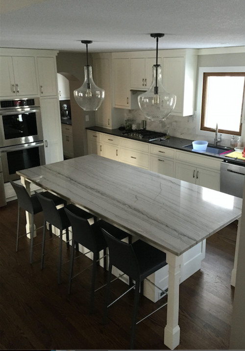 Example of a large transitional dark wood floor and brown floor kitchen design in Minneapolis with an undermount sink, shaker cabinets, white cabinets, gray backsplash, stone tile backsplash, stainless steel appliances, an island and solid surface countertops