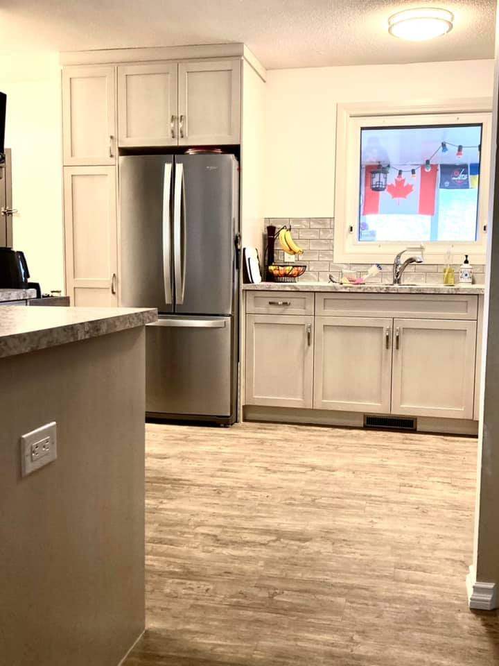 Open concept kitchen - mid-sized transitional l-shaped vinyl floor and beige floor open concept kitchen idea with a drop-in sink, shaker cabinets, beige cabinets, laminate countertops, gray backsplash, ceramic backsplash, stainless steel appliances, an island and multicolored countertops