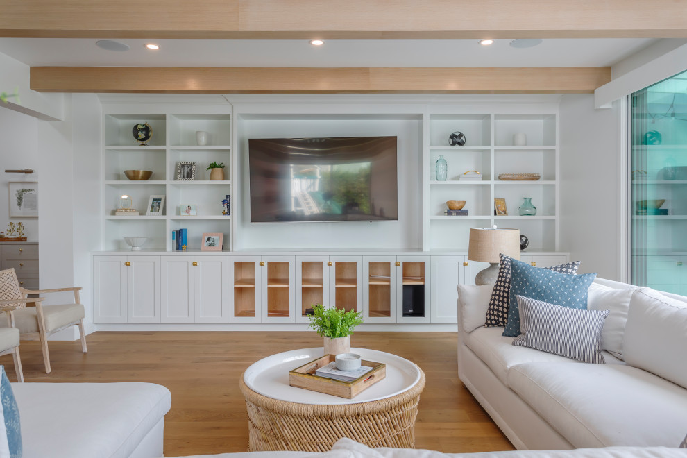This is an example of a large beach style open concept living room in Los Angeles with white walls, medium hardwood floors, a built-in media wall and beige floor.