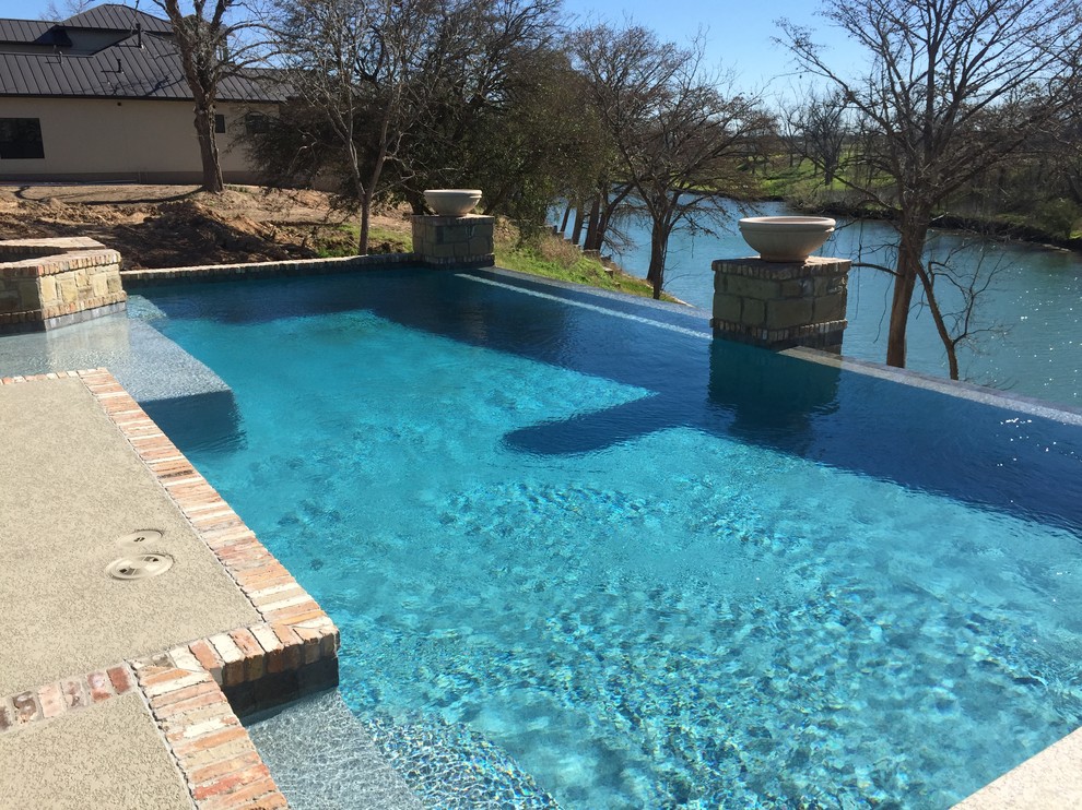 Mid-sized backyard stamped concrete and custom-shaped infinity hot tub photo in Austin