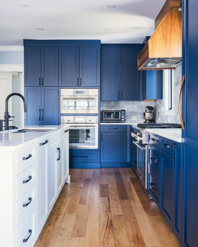 Bild på ett vintage vit vitt l-kök, med en undermonterad diskho, skåp i shakerstil, blå skåp, marmorbänkskiva, grått stänkskydd, stänkskydd i stenkakel, rostfria vitvaror, mellanmörkt trägolv, en köksö och brunt golv