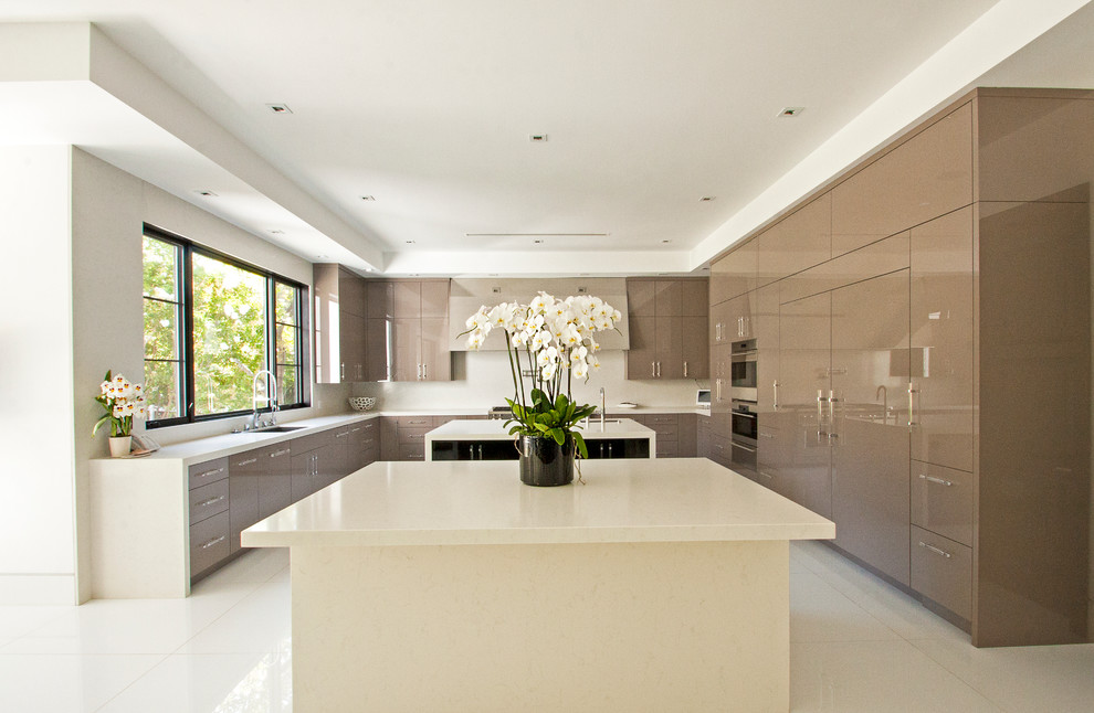 Expansive modern u-shaped eat-in kitchen in Los Angeles with an undermount sink, flat-panel cabinets, beige cabinets, solid surface benchtops, stainless steel appliances, marble floors and multiple islands.