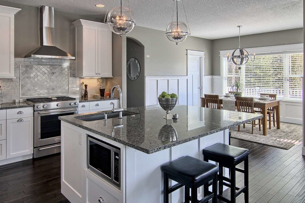 Example of a mid-sized transitional l-shaped dark wood floor open concept kitchen design with a single-bowl sink, shaker cabinets, white cabinets, granite countertops, gray backsplash, stone tile backsplash, stainless steel appliances and an island