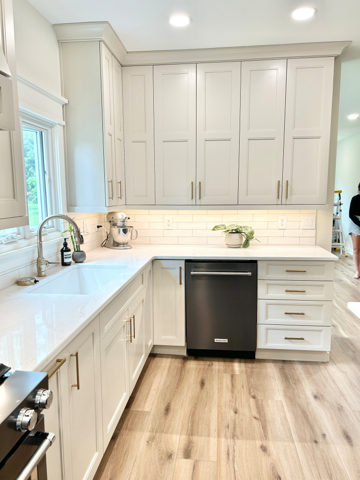Open concept kitchen - large transitional u-shaped light wood floor open concept kitchen idea with an undermount sink, flat-panel cabinets, white cabinets, quartz countertops, white backsplash, ceramic backsplash, black appliances, an island and white countertops